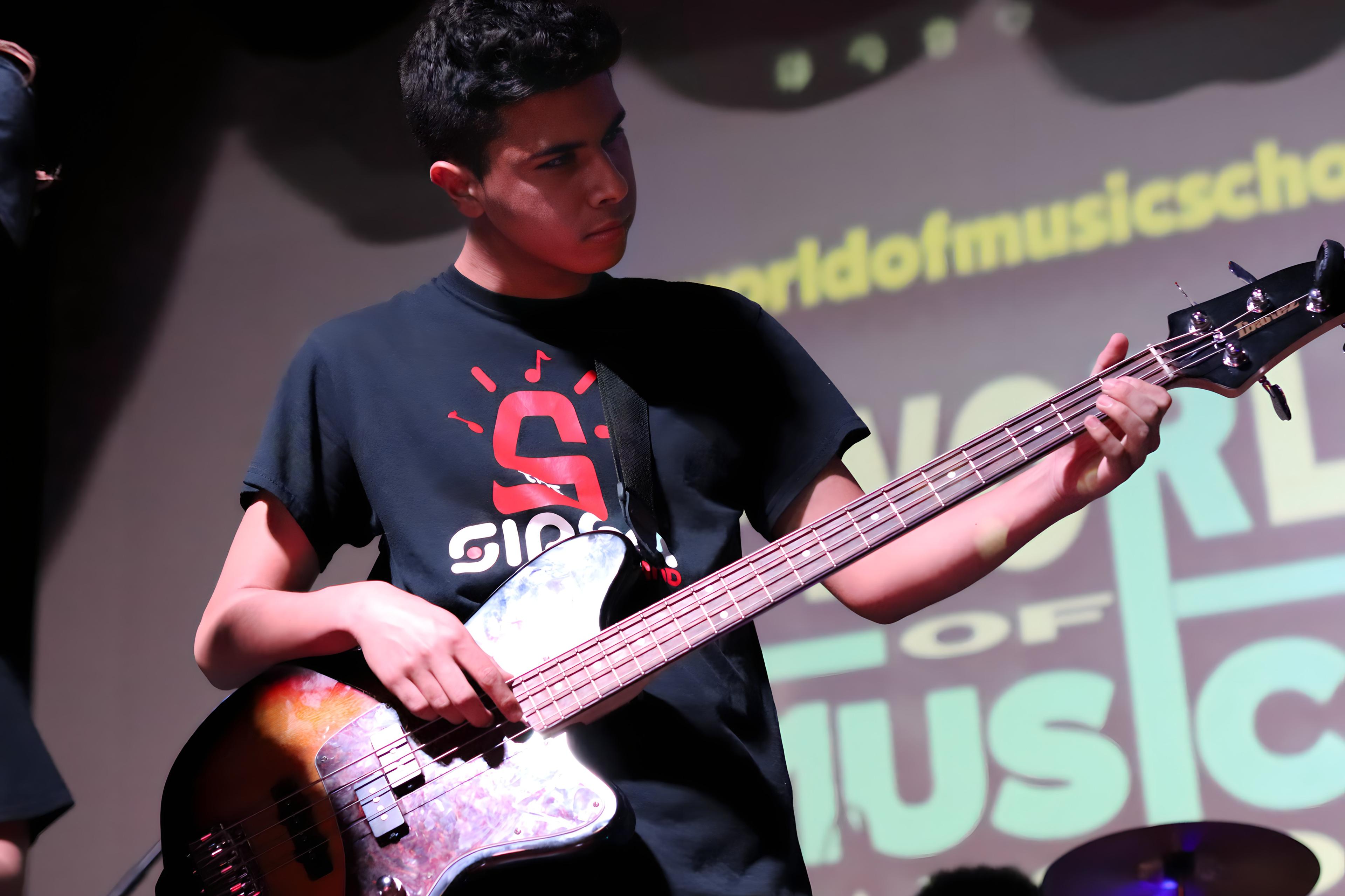 Teen playing bass guitar on stage with TWOM backdrop