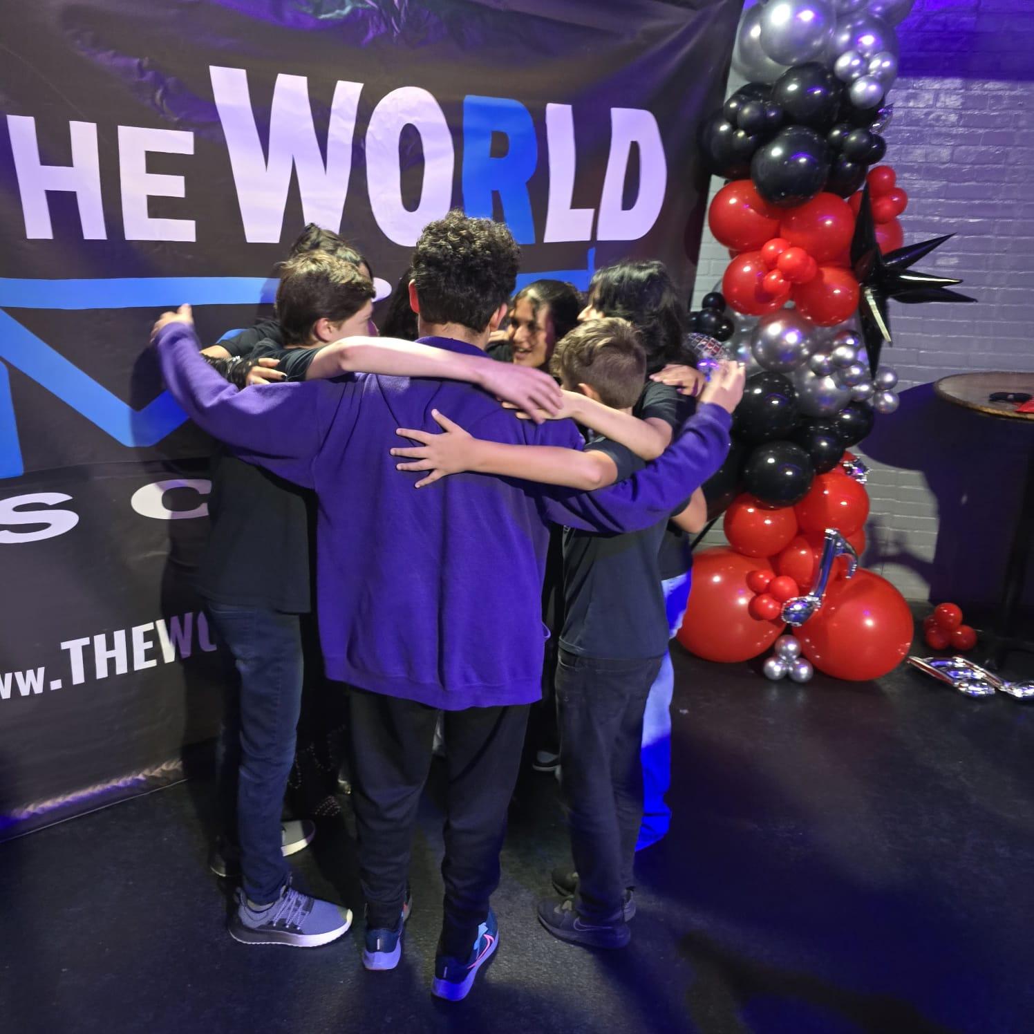 Students group hug with TWOM banner and balloons
