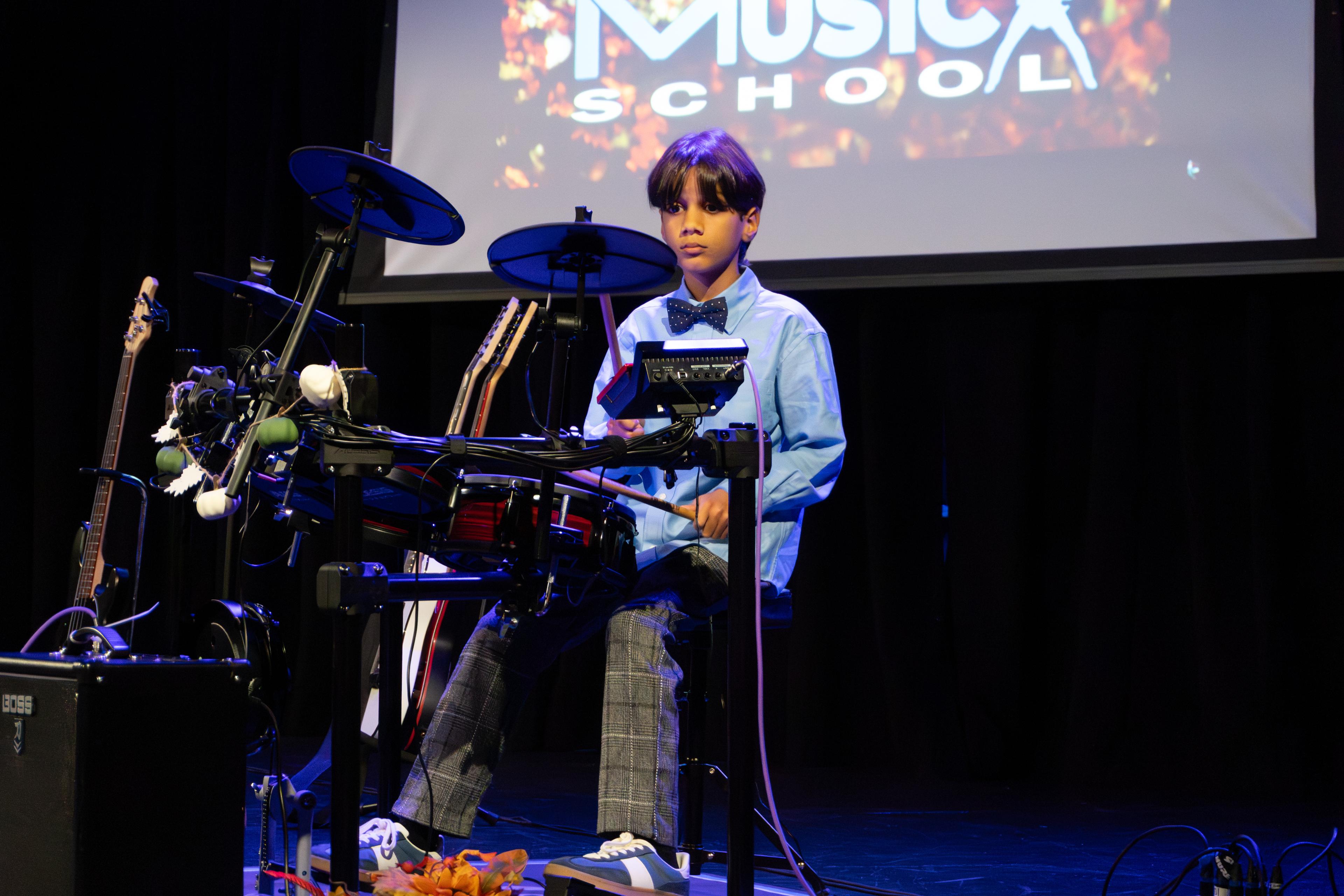 Young boy in blue shirt performing drums at fall recital