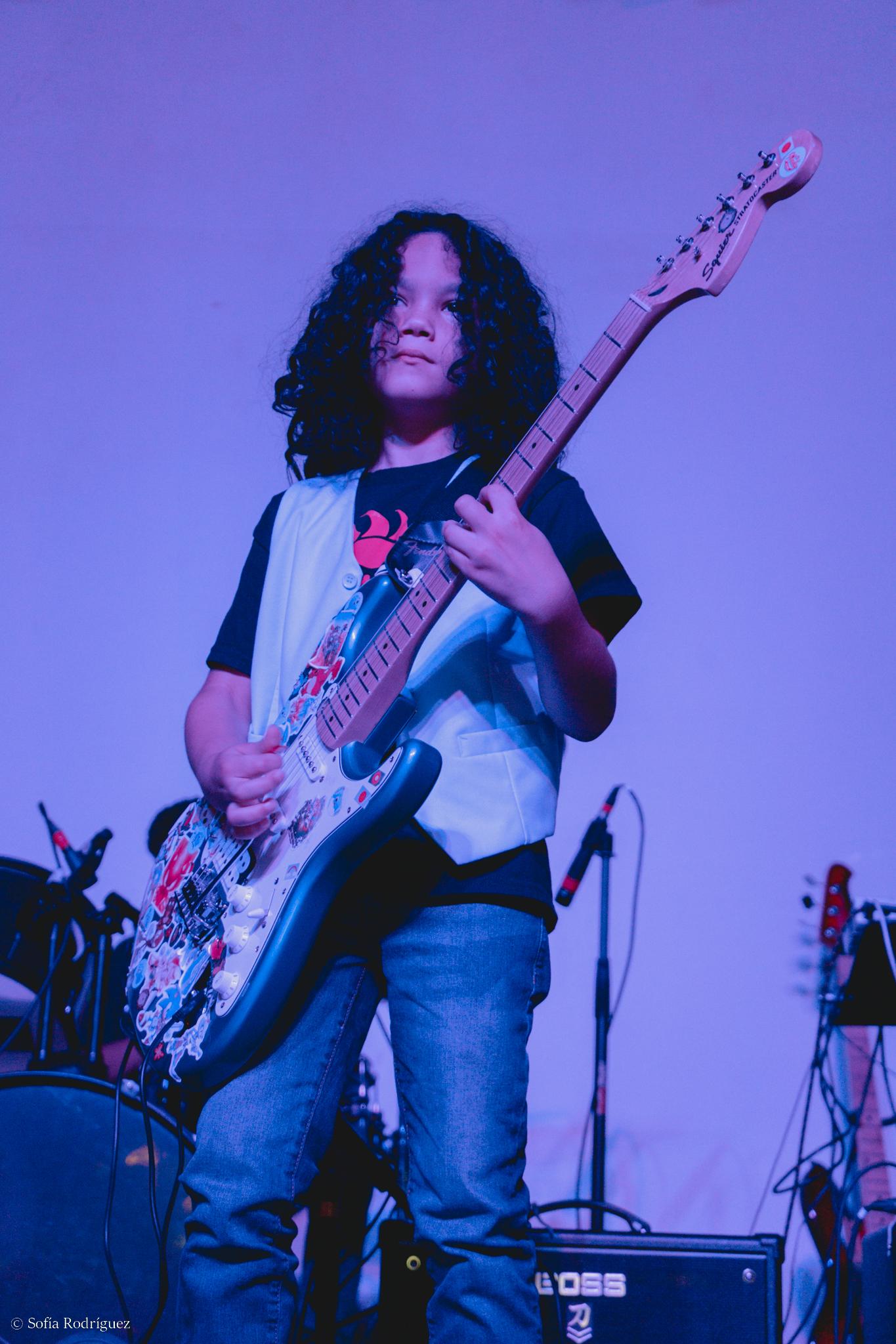 Student performing electric guitar on purple-lit stage